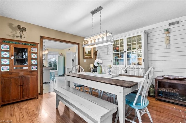 dining space featuring light hardwood / wood-style flooring, wooden walls, and a textured ceiling