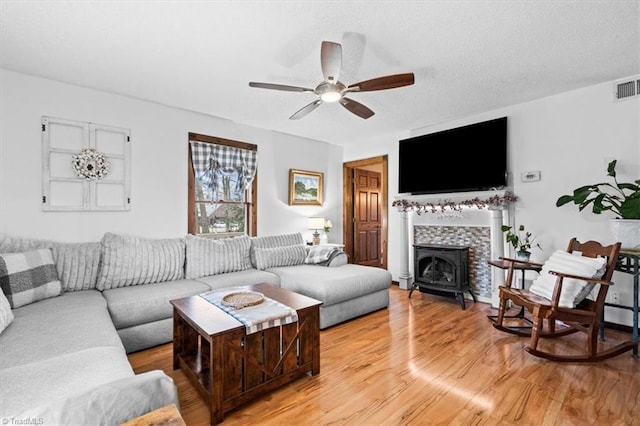 living room featuring a wood stove, a textured ceiling, ceiling fan, and light hardwood / wood-style flooring