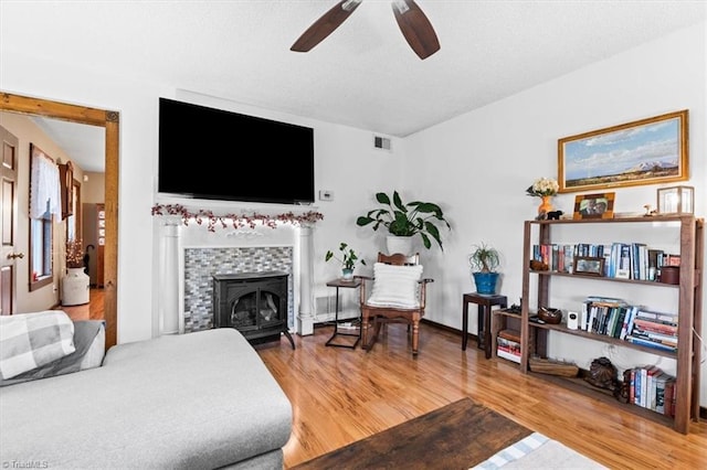 living room featuring wood-type flooring, ceiling fan, and a wood stove