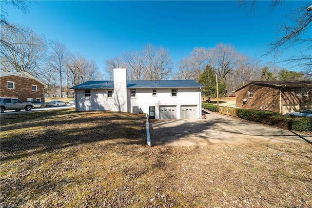 rear view of property featuring an attached garage, metal roof, driveway, and a chimney