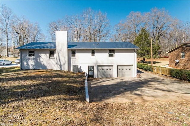 back of property with a chimney, an attached garage, metal roof, and central AC