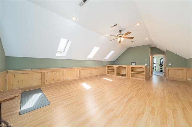 additional living space featuring a ceiling fan, vaulted ceiling with skylight, visible vents, and light wood-style flooring