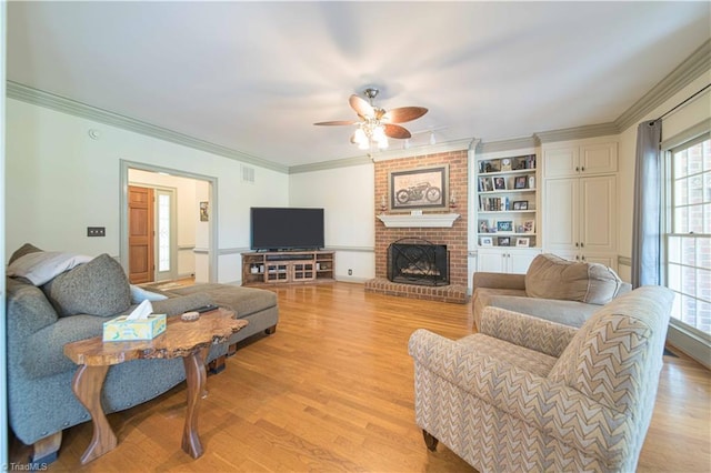 living area featuring light wood-style flooring, visible vents, ceiling fan, a fireplace, and ornamental molding