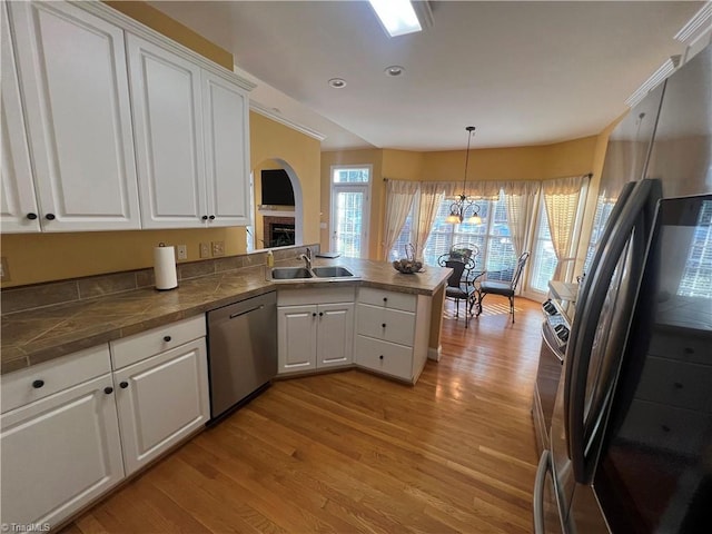 kitchen with white cabinetry, stainless steel appliances, sink, hanging light fixtures, and kitchen peninsula