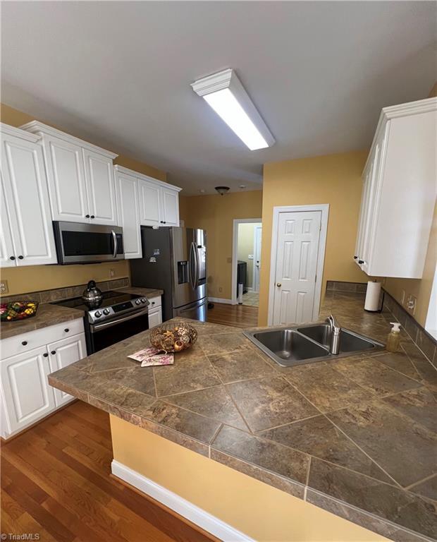 kitchen featuring kitchen peninsula, stainless steel appliances, dark hardwood / wood-style floors, white cabinets, and sink