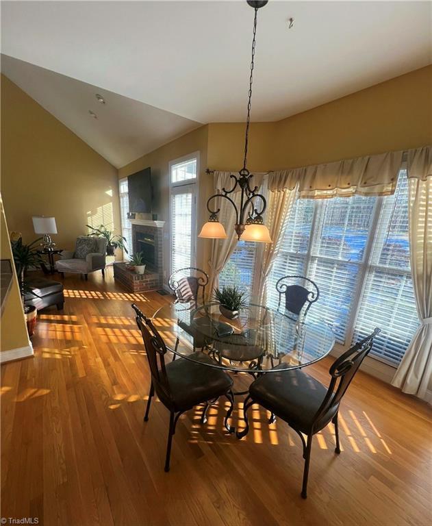 dining room featuring lofted ceiling, a fireplace, an inviting chandelier, and hardwood / wood-style floors