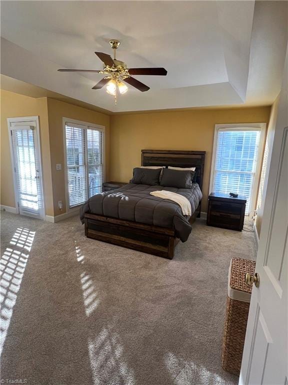 bedroom with ceiling fan, access to exterior, carpet, and a tray ceiling