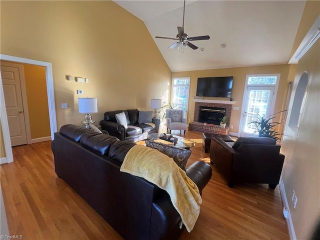 living room with ceiling fan, lofted ceiling, a brick fireplace, and light hardwood / wood-style flooring