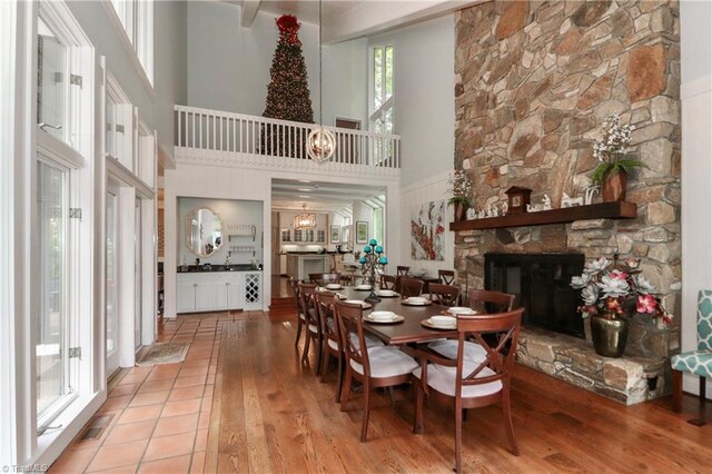 dining room with a towering ceiling, a stone fireplace, and light hardwood / wood-style flooring