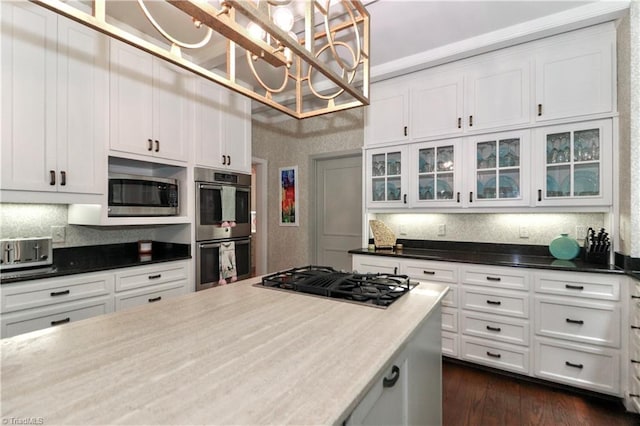 kitchen with appliances with stainless steel finishes, dark countertops, white cabinetry, and glass insert cabinets