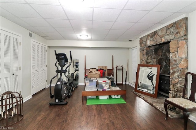 exercise room featuring visible vents, dark wood-type flooring, a paneled ceiling, and baseboards