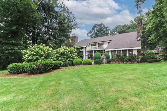 view of front of property featuring a balcony, a chimney, and a front lawn