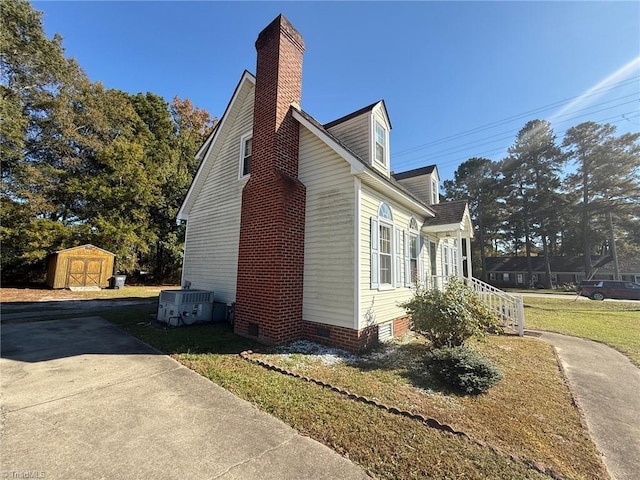 view of home's exterior with central AC unit, a storage shed, an outdoor structure, crawl space, and a chimney