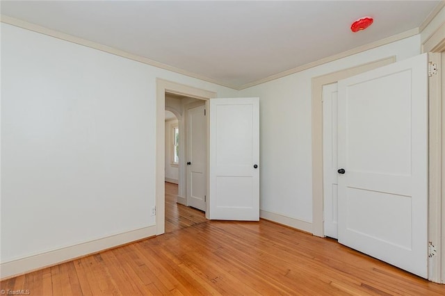 spare room featuring ornamental molding, arched walkways, light wood-style flooring, and baseboards