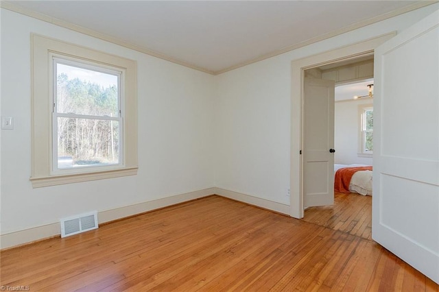 spare room with light wood-type flooring, visible vents, crown molding, and baseboards