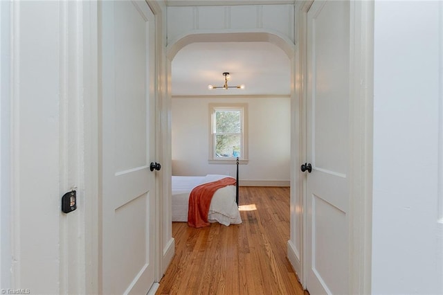 hall with arched walkways, light wood-style flooring, and baseboards