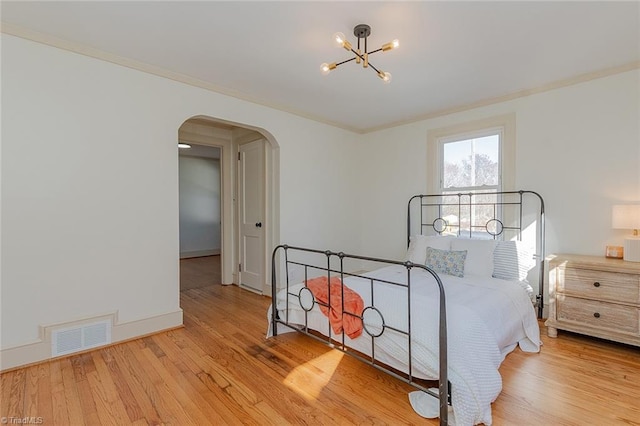 bedroom featuring light wood-style floors, visible vents, arched walkways, and ornamental molding