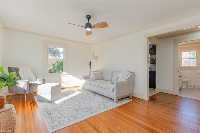 living area with a healthy amount of sunlight, visible vents, crown molding, and light wood finished floors