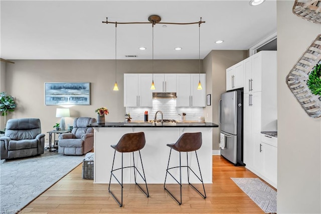 kitchen featuring dark countertops, a breakfast bar area, open floor plan, freestanding refrigerator, and backsplash