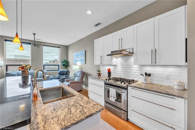 kitchen with backsplash, white cabinetry, a sink, stainless steel gas range, and under cabinet range hood