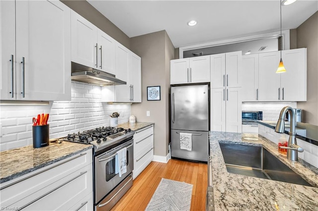 kitchen with light stone counters, under cabinet range hood, stainless steel appliances, a sink, and white cabinetry