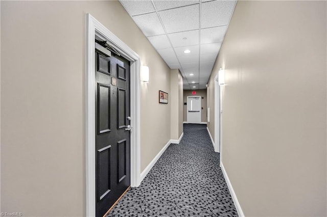 corridor with dark colored carpet, a drop ceiling, baseboards, and recessed lighting