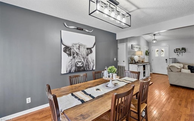 dining room with a textured ceiling, hardwood / wood-style floors, lofted ceiling, and baseboards