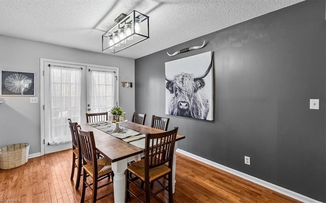 dining room featuring a textured ceiling, baseboards, wood finished floors, and french doors