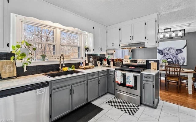 kitchen with appliances with stainless steel finishes, marble finish floor, gray cabinets, under cabinet range hood, and a sink