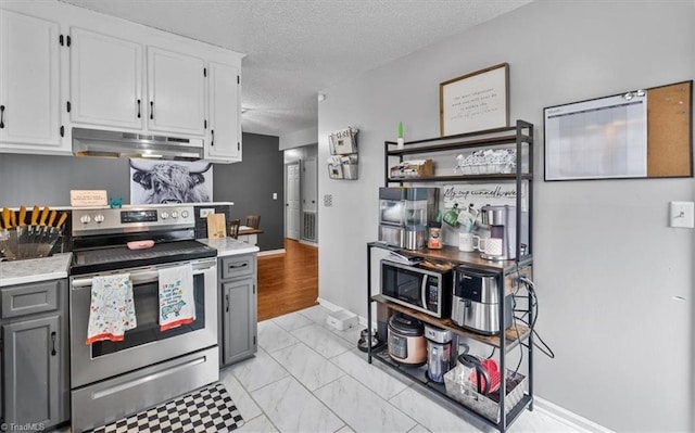 kitchen featuring a textured ceiling, under cabinet range hood, white cabinetry, marble finish floor, and appliances with stainless steel finishes