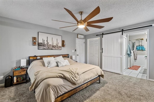 carpeted bedroom with a barn door, a ceiling fan, a textured ceiling, and ensuite bathroom