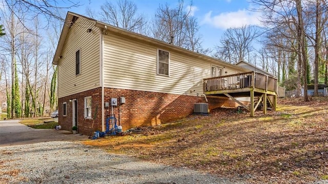 view of side of home with cooling unit, gravel driveway, brick siding, and a deck