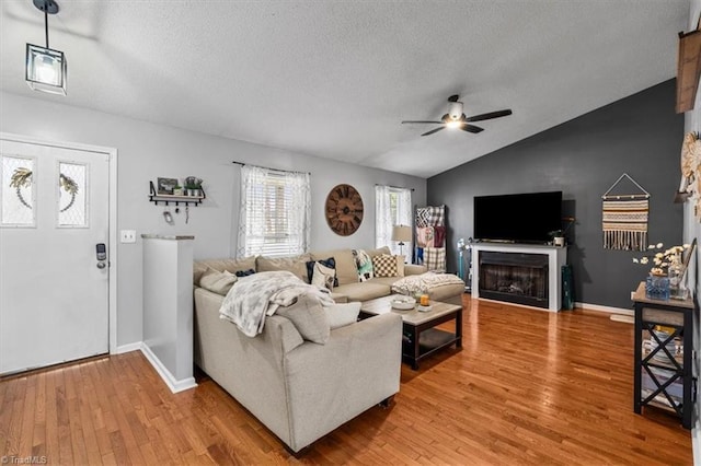 living area featuring a ceiling fan, vaulted ceiling, a textured ceiling, light wood-type flooring, and a fireplace