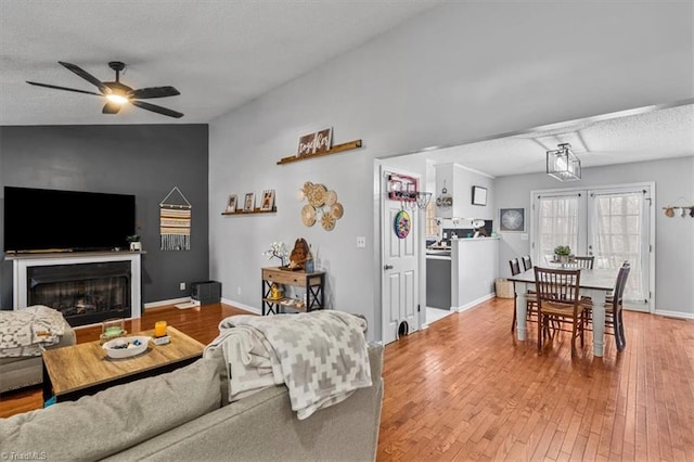 living room with a fireplace, a ceiling fan, a textured ceiling, baseboards, and hardwood / wood-style flooring