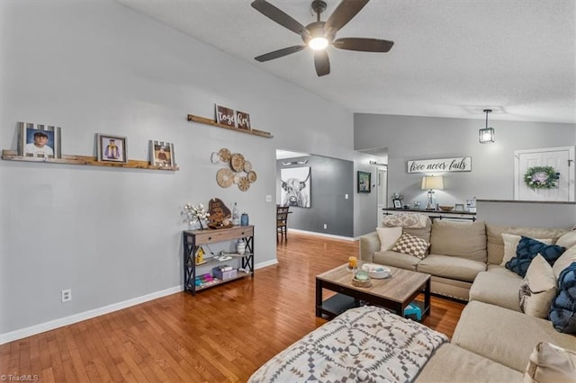 living room with baseboards, a ceiling fan, wood finished floors, vaulted ceiling, and a textured ceiling