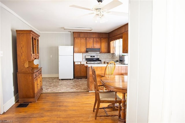 319 Cherry St, Eden, NC 27288 - kitchen with stainless steel range with gas stovetop, under cabinet range hood, ceiling fan, freestanding refrigerator, and brown cabinets