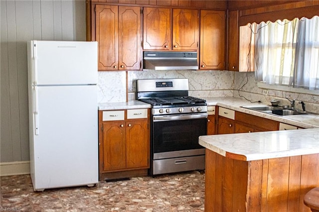 319 Cherry St, Eden, NC 27288 - kitchen with stainless steel range with gas stovetop, under cabinet range hood, a sink, freestanding refrigerator, and brown cabinets