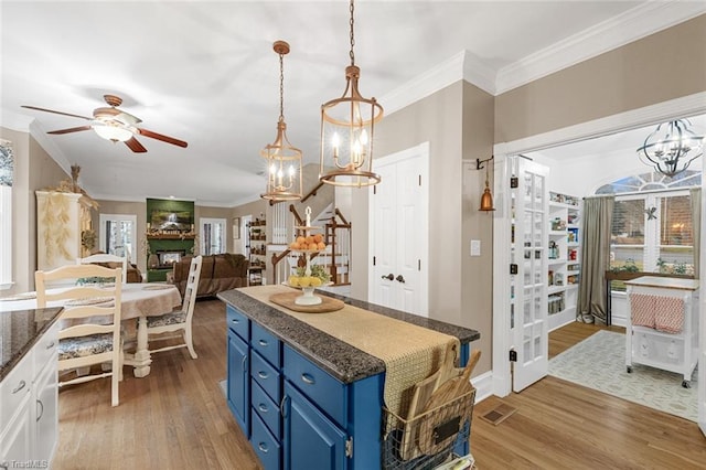 kitchen with crown molding, light hardwood / wood-style flooring, ceiling fan with notable chandelier, and blue cabinets