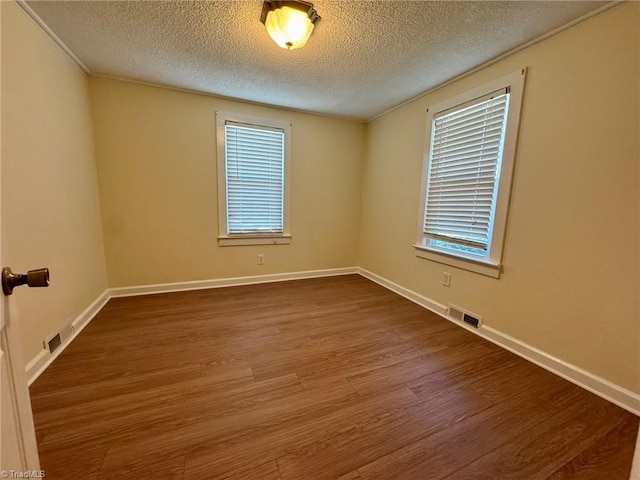 empty room with wood finished floors, a textured ceiling, and visible vents