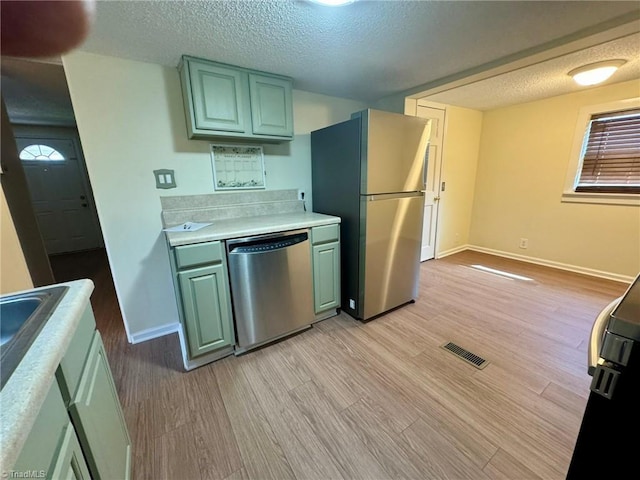 kitchen featuring baseboards, stainless steel appliances, light wood finished floors, and light countertops