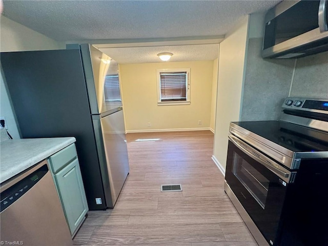 kitchen featuring a textured ceiling, light wood finished floors, stainless steel appliances, and visible vents