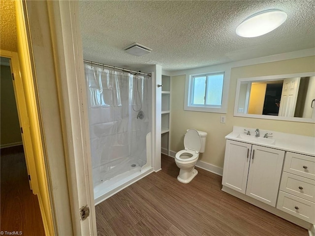 bathroom with a shower stall, wood finished floors, toilet, vanity, and a textured ceiling