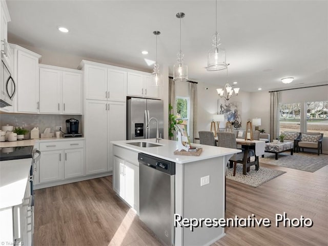 kitchen with light wood-type flooring, an island with sink, a sink, appliances with stainless steel finishes, and light countertops