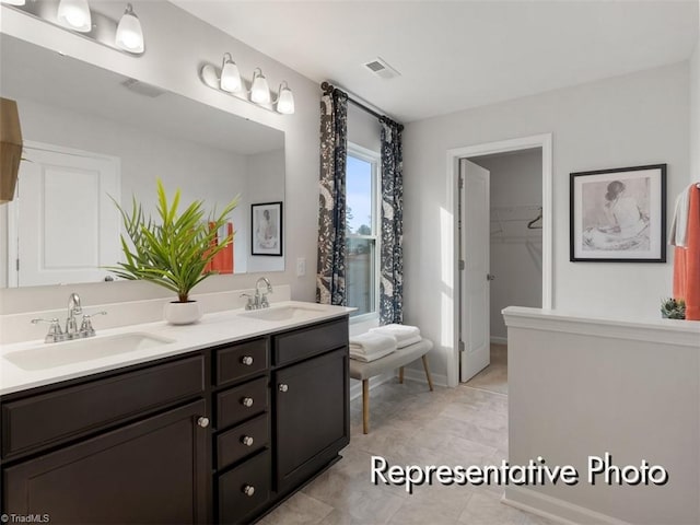 bathroom with double vanity, visible vents, a walk in closet, and a sink