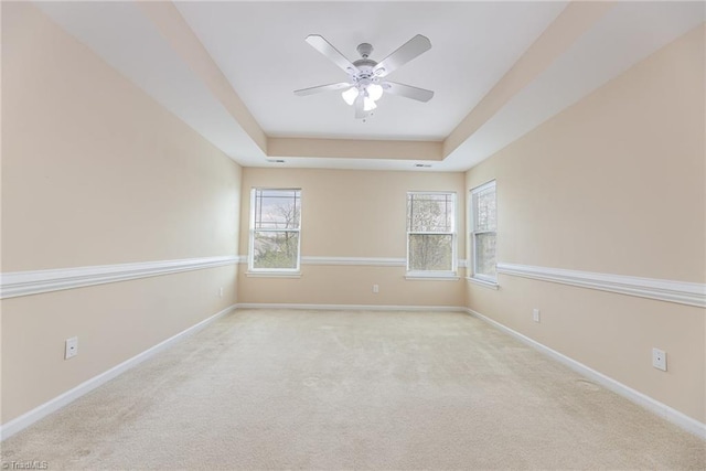 spare room with a raised ceiling, carpet, baseboards, and ceiling fan