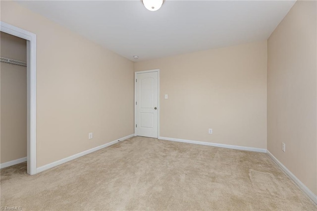 unfurnished bedroom with a closet, light colored carpet, and baseboards