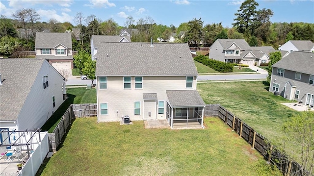 rear view of house featuring a sunroom, central air condition unit, a yard, a fenced backyard, and a residential view