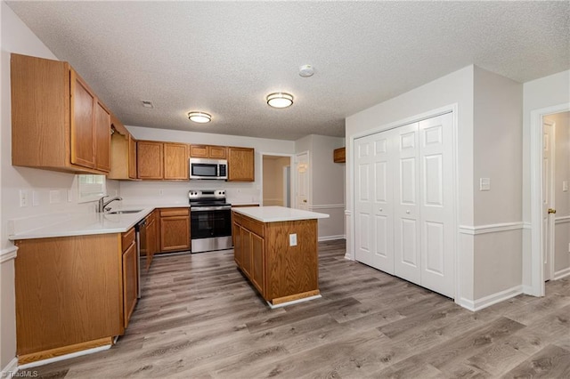 5207 Highland Oak Ct, Greensboro, NC 27410 - kitchen with stainless steel appliances, light wood-style floors, a kitchen island, brown cabinets, and a textured ceiling