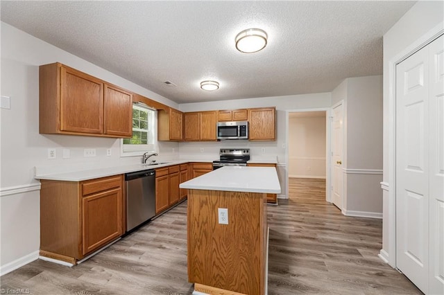 5207 Highland Oak Ct, Greensboro, NC 27410 - kitchen featuring appliances with stainless steel finishes, light wood-style floors, light countertops, a textured ceiling, and brown cabinets