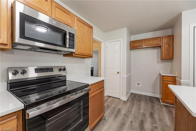 5207 Highland Oak Ct, Greensboro, NC 27410 - kitchen with appliances with stainless steel finishes, light countertops, brown cabinetry, light wood-style floors, and a textured ceiling